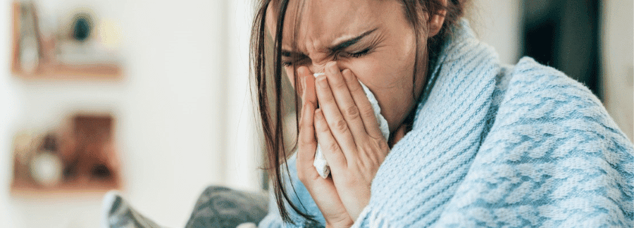 Hoe ga je om met winterkwaaltjes? Zieke vrouw die haar neus snuit